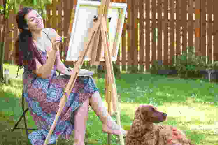 woman painting on easel outside with dog