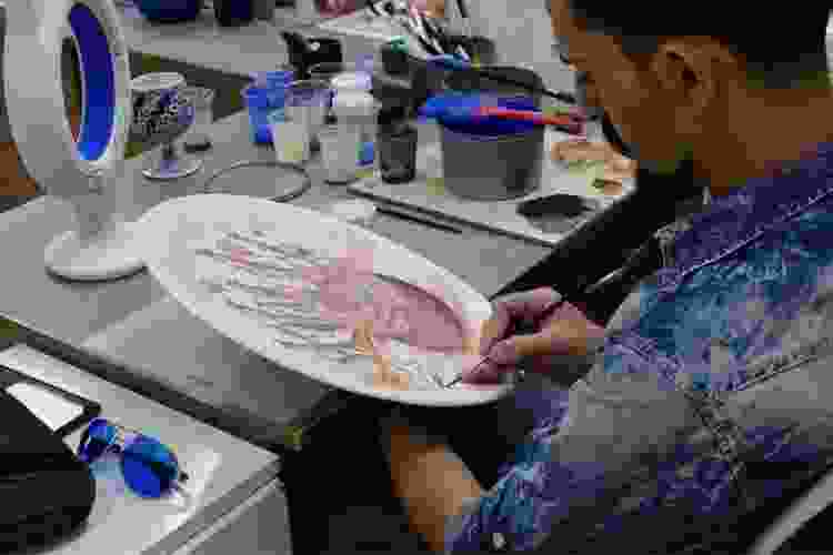 man painting ceramic design on large plate