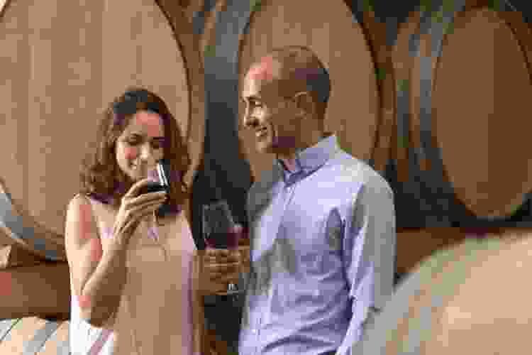 couple smelling wine surrounded by wine barrels