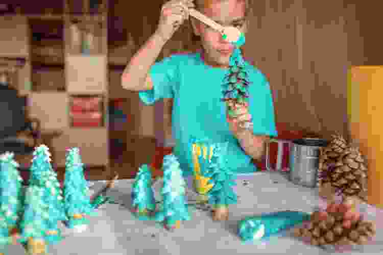 young child painting pinecones as Christmas trees