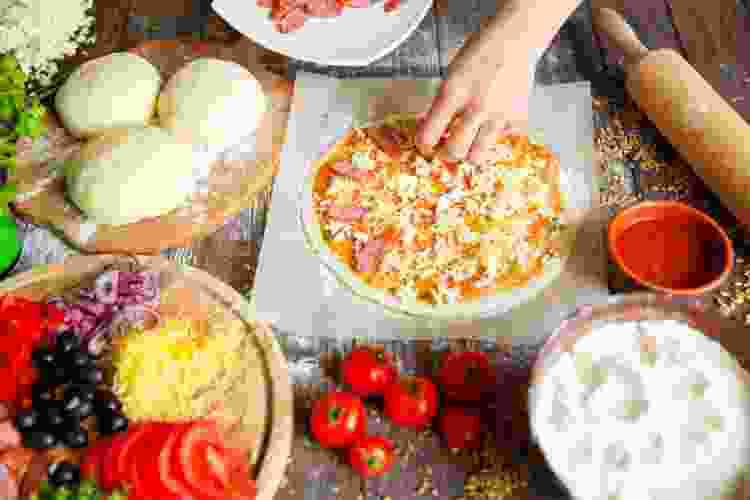 hand spreading toppings on pizza dough