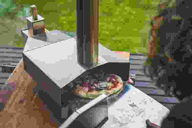 person cooking over wood-fired pizza oven outdoors