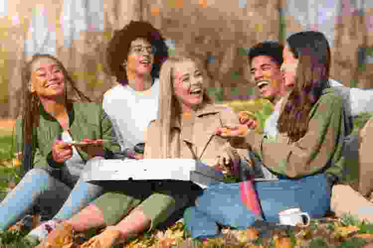 group of teens eating pizza in the park