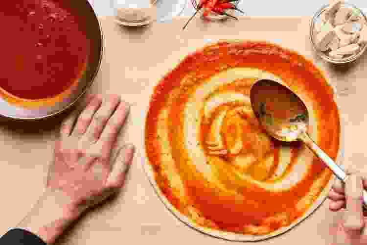 ladle spreading pizza sauce on dough