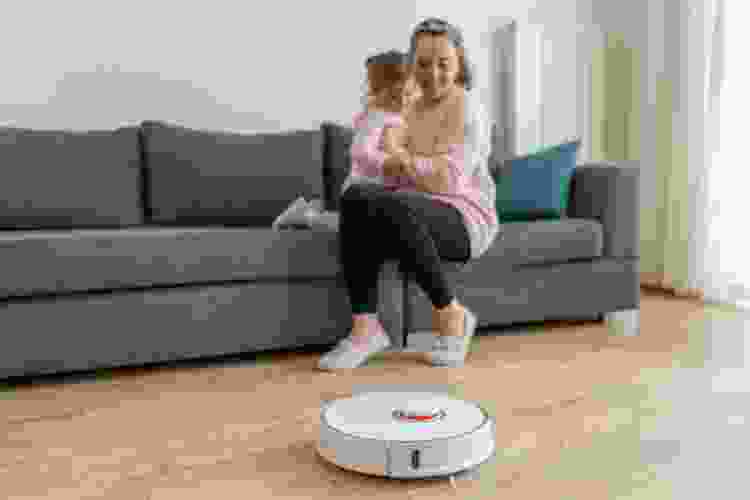 woman with child watching robot vacuum on floor