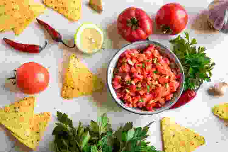 bowl of salsa surrounded by tortilla chips and tomatoes