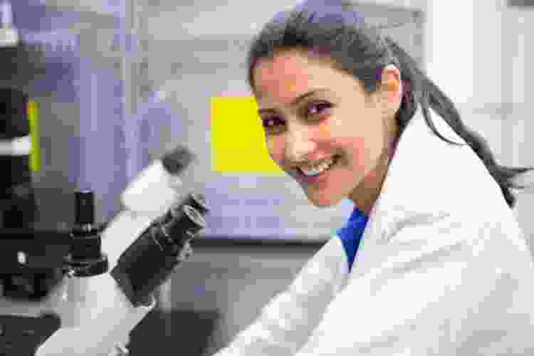 scientist wearing lab coat and smiling next to microscope