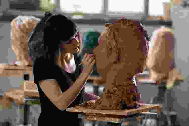 woman carving face sculpture out of clay