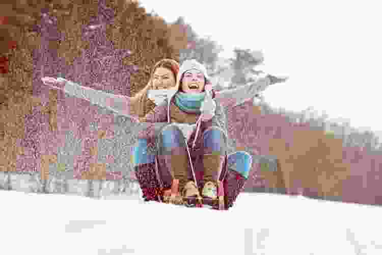 two women laughing on sled in snow