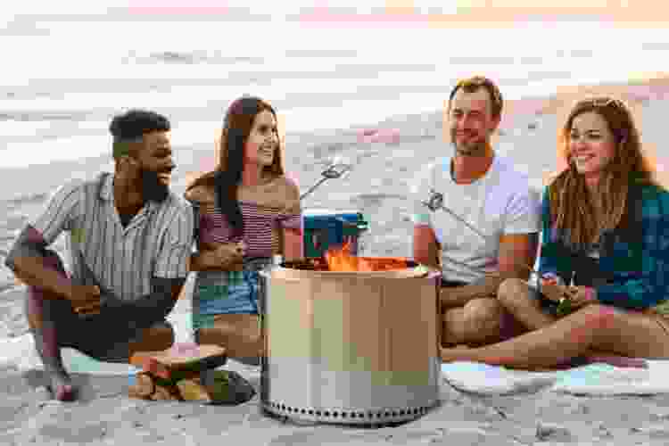 group of friends gathered around solo stove on the beach