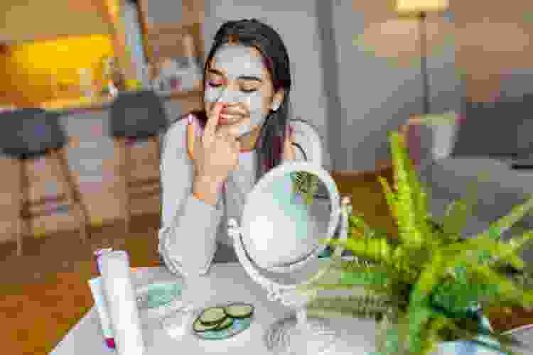 young woman applying mud mask in home spa