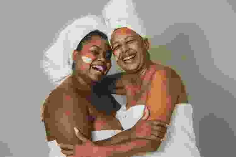 mother and daughter hugging in towels and mud masks at the spa