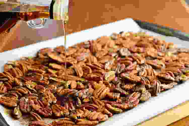 pouring maple syrup on baking sheet of pecans