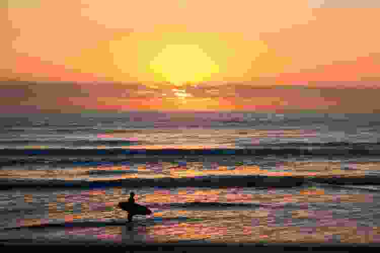 Surfer standing in the ocean at sunset