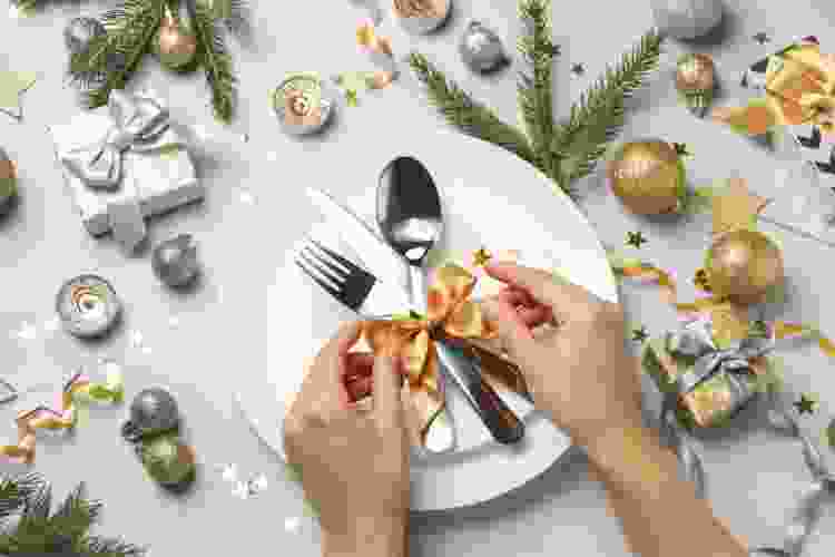 hands tying ribbon around dinnerware and linen 