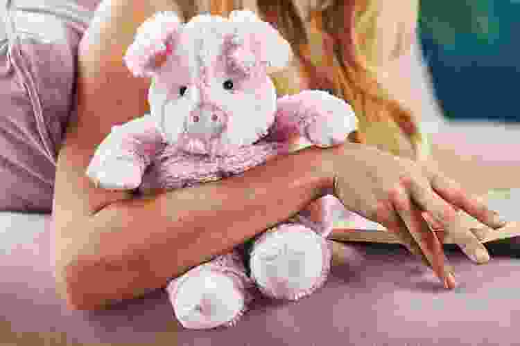 woman reading while snuggling heated stuffed animal pig