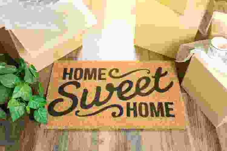 home sweet home welcome mat surrounded by moving boxes