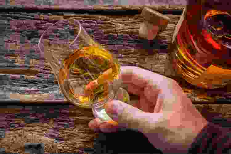 holding small whiskey tasting glass next to bottle of whiskey