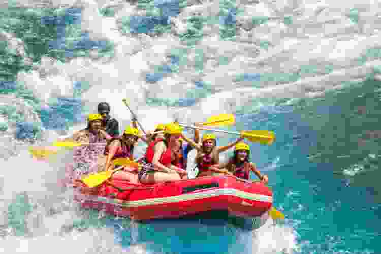 group of friends riding raft down river rapids