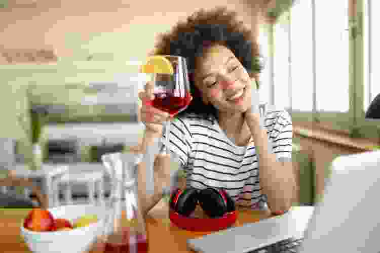 woman sipping sangria while video chatting on laptop