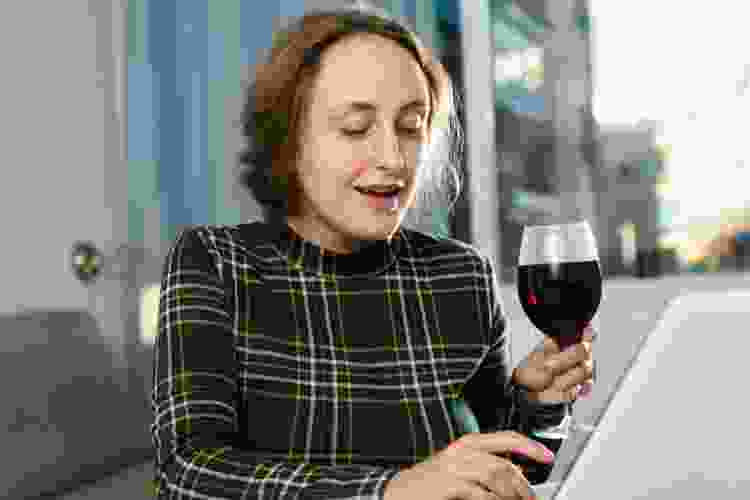 woman drinking wine while using laptop