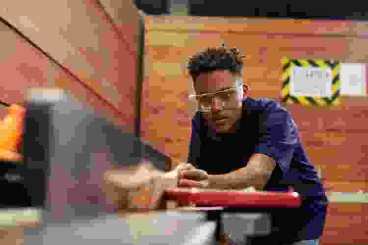 young man sawing wood in woodshop