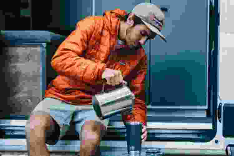 young man outdoors pouring coffee into YETI rambler cup