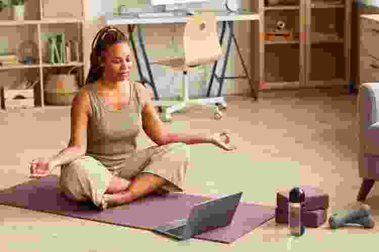 woman meditating with laptop and yoga mat at home