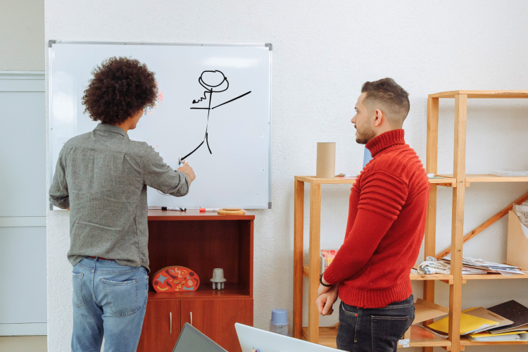 Two men playing pictionary on a white board