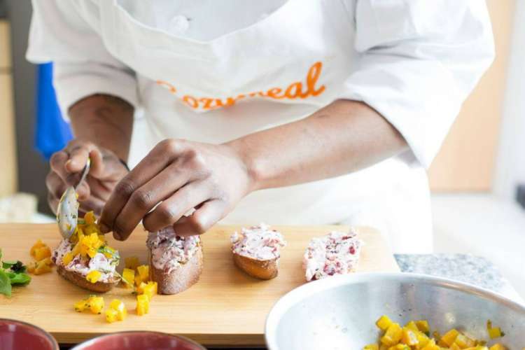 Close-up of a chef's (wearing a Cozymeal apron) hands making food