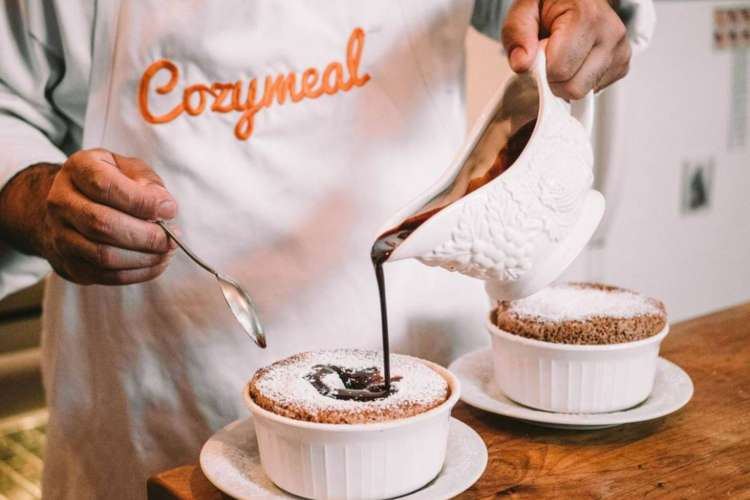 a chef in a Cozymeal apron garnishes a dessert with chocolate syrup