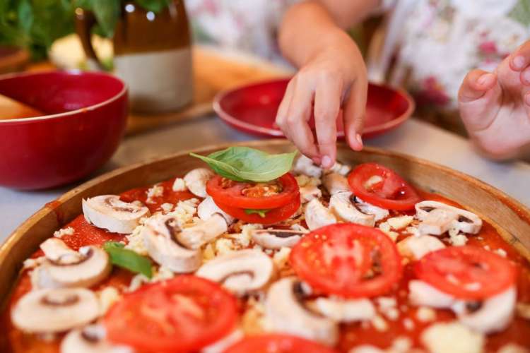 a hand garnishing a pizza with a basil leaf