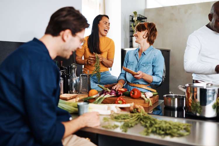 three people laughing and chopping vegetables together