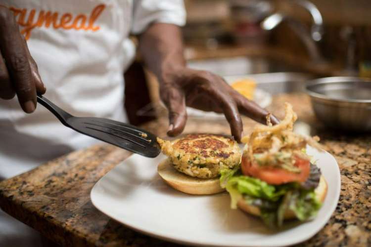 a chef wearing a Cozymeal apron plates a veggie burger