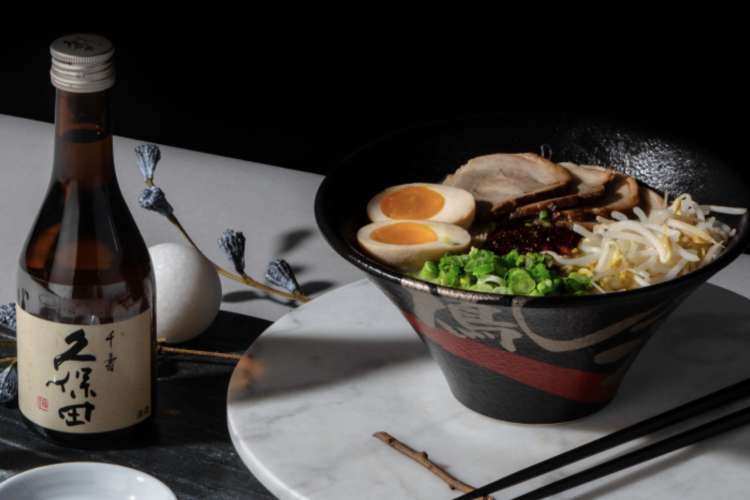 a bowl of ramen and a bottle of sake on a table