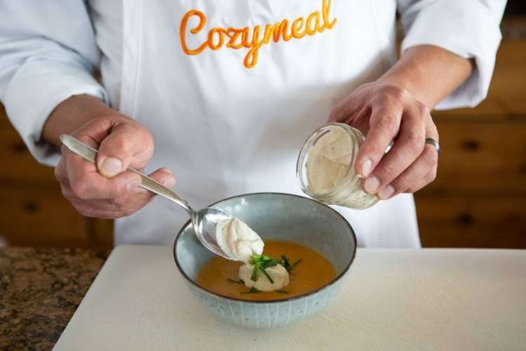 a chef in a Cozymeal apron garnishing a dish