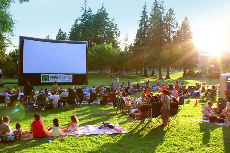 people of various ages in front of an outdoor screen on a sunny day