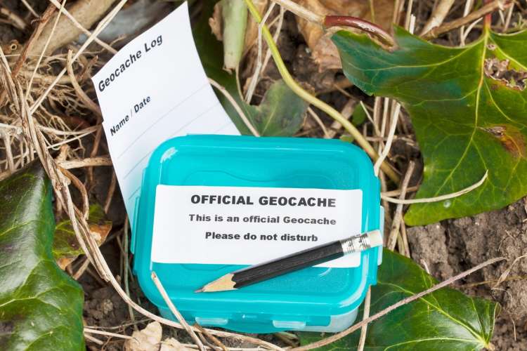 a blue-lidded geocache box in the grass with a do not disturb sign on it