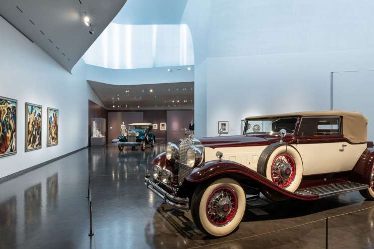 an antique car sitting in a large room with art-lined walls