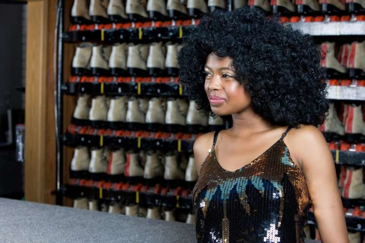 a smiling woman before a wall of roller skates at a rink