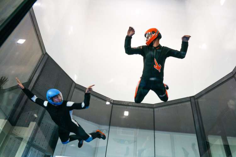 two people in protective gear hovering in the air during indoor skydiving