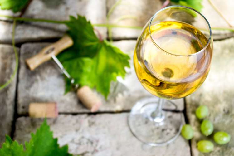 a glass of white wine with grapes and corkscrew