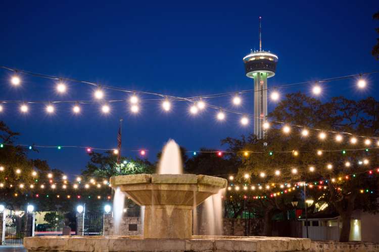 view of Tower of the Americas and a fountain at dusk with lights strung overhead