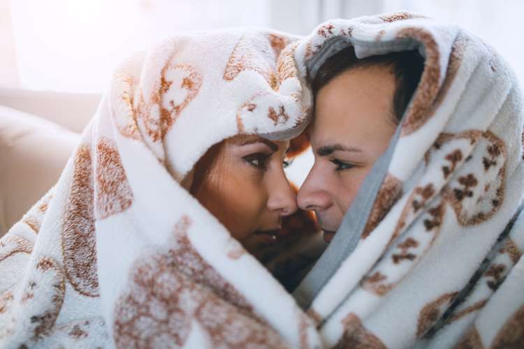 a man and woman cuddle under a plush blanket