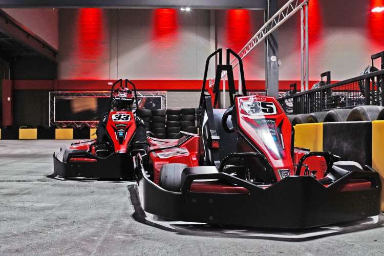 two large red race cars sit in an indoor raceway