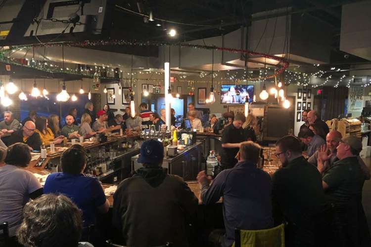 a large group of people around a bar in a bright, cheerful distillery