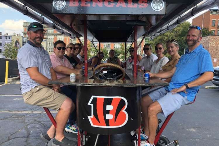 twelve people smiling for a photo while sitting in a pedal wagon