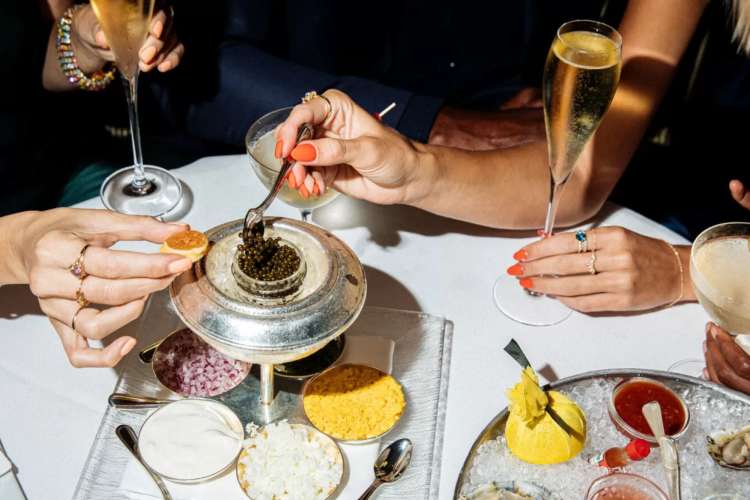 two women spooning out caviar and holding drinks