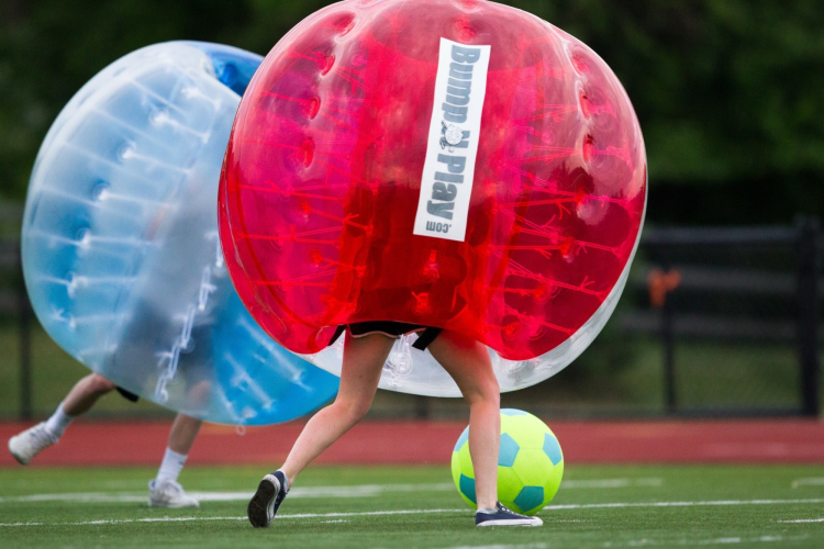 People wrapped in giant bubbles playing soccer outdoors.