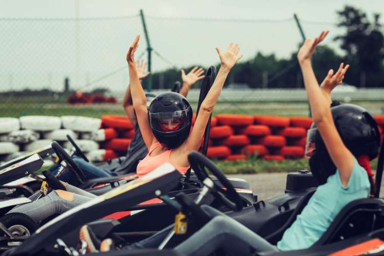 a helmeted woman in a go-kart raises her arms overhead in triumph